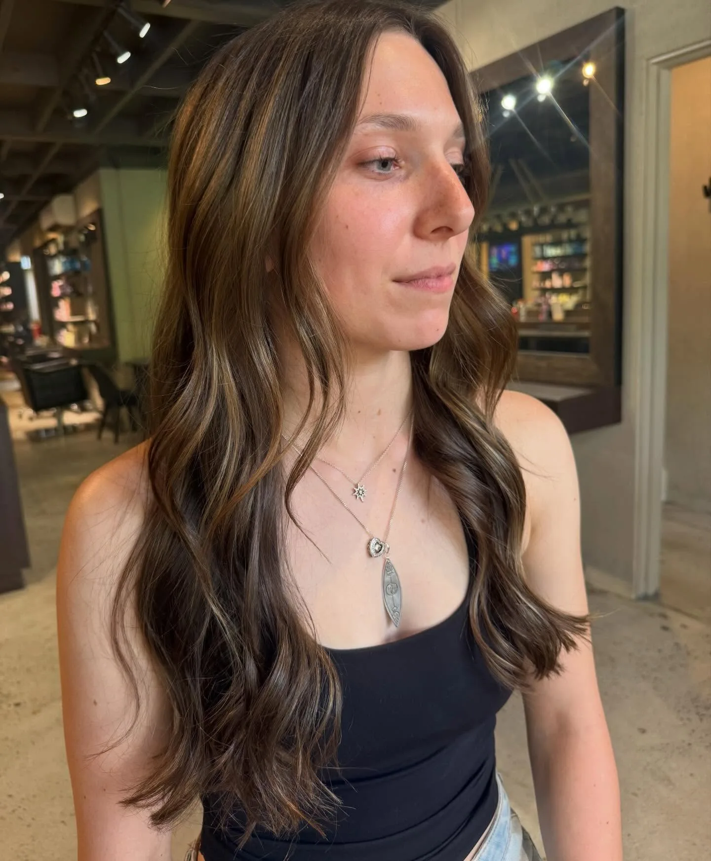 Brunette balayage long waves, client profile — salon floor behind