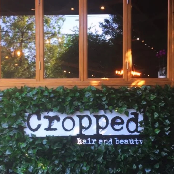 Illuminated storefront window — the Cropped wordmark plaque above an ivy-hedge at night, Ringwood