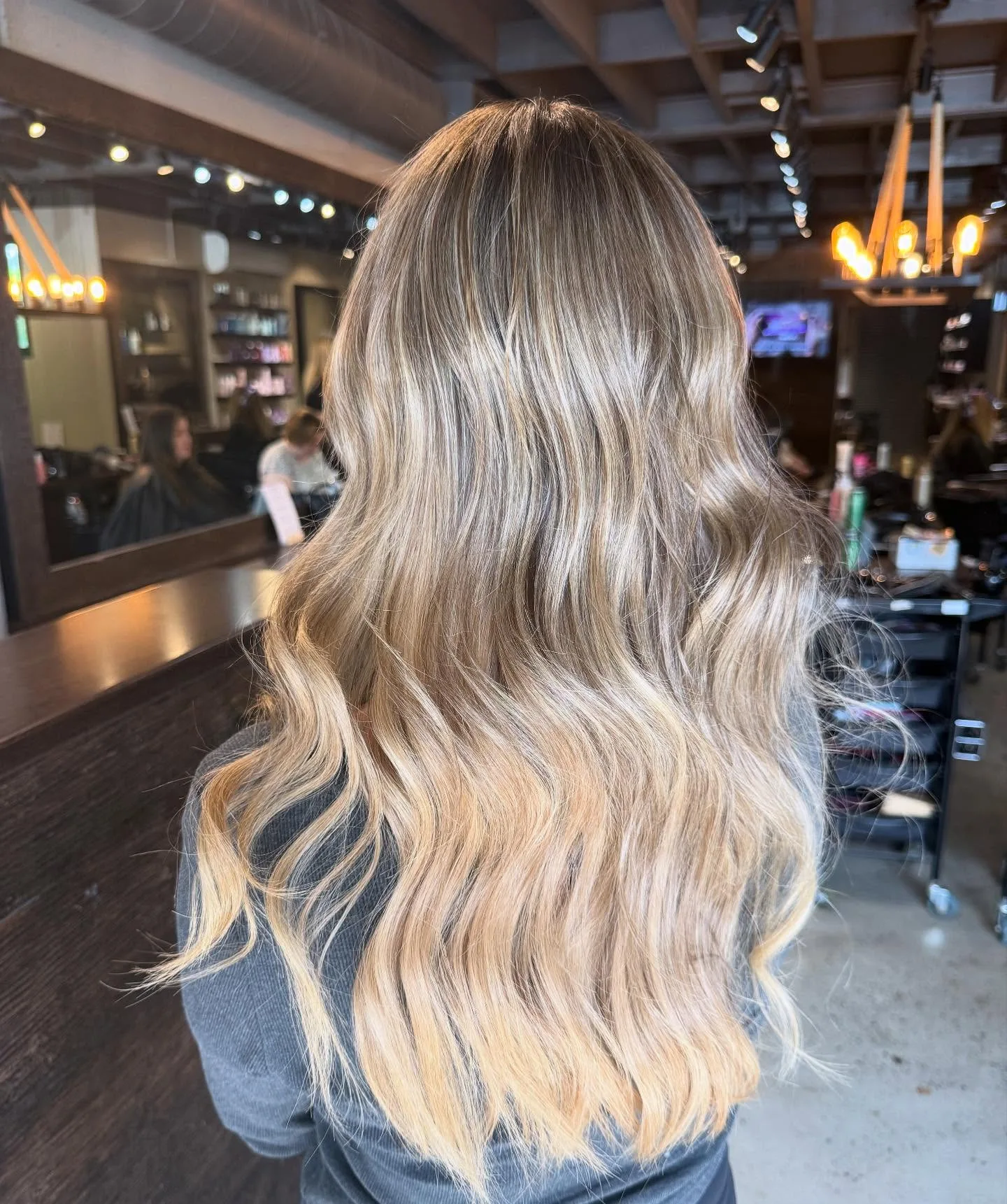 Long lived-in blonde balayage, rear view, warm Cropped salon interior with Edison chandelier