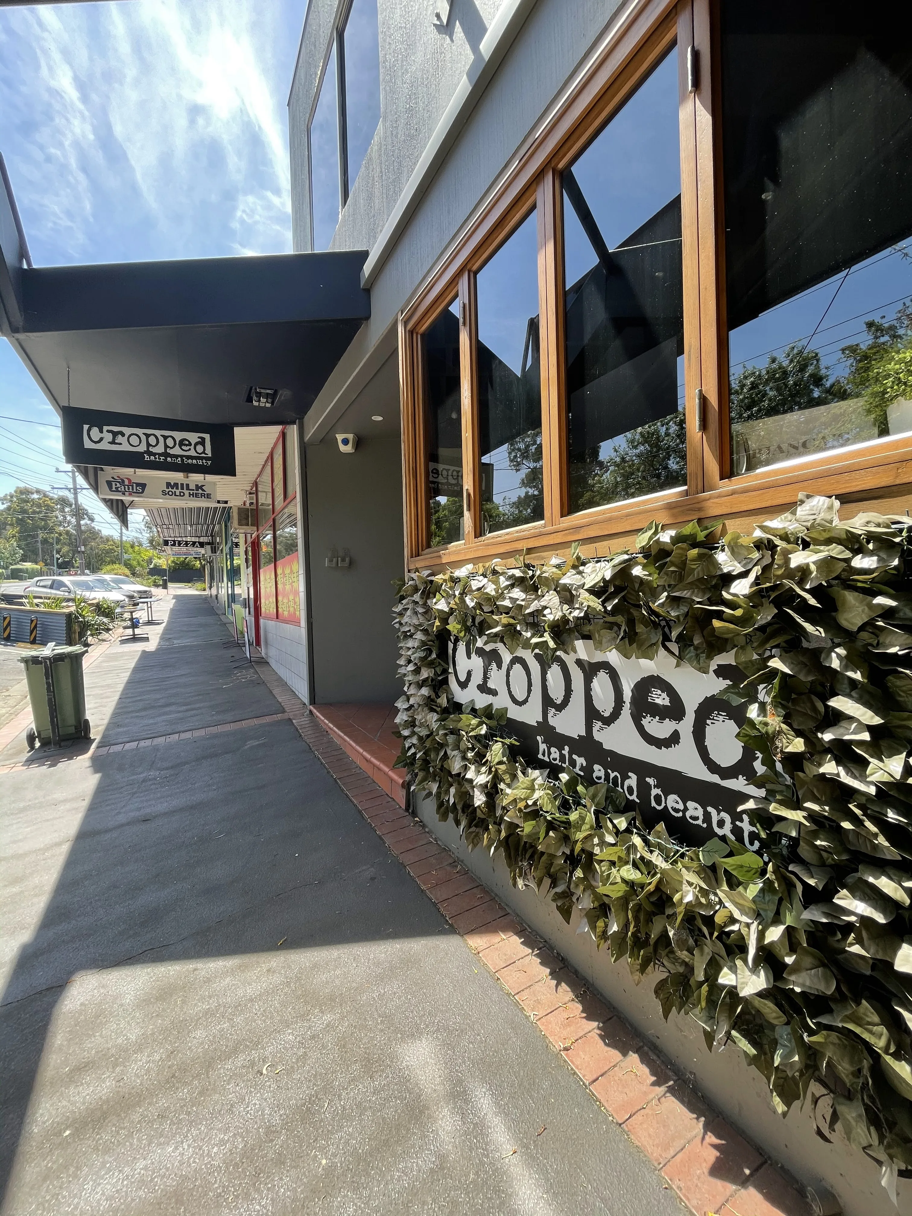 Cropped Hair and Beauty daytime streetscape — timber shopfront, black awning, ivy-hedge wordmark plaque, Loughnan Road Ringwood
