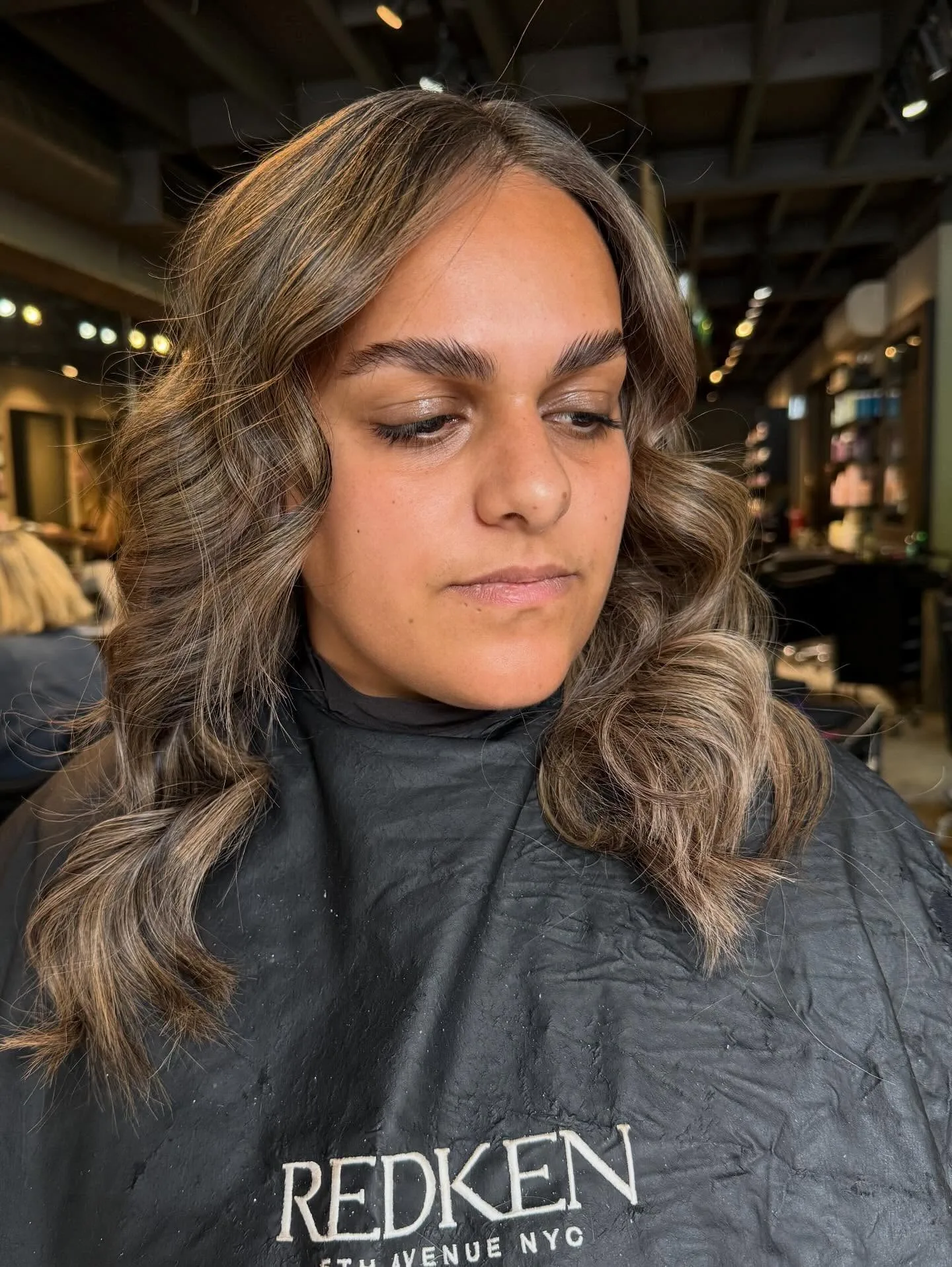 Bronde balayage with laminated brows, client face — Redken cape, salon interior