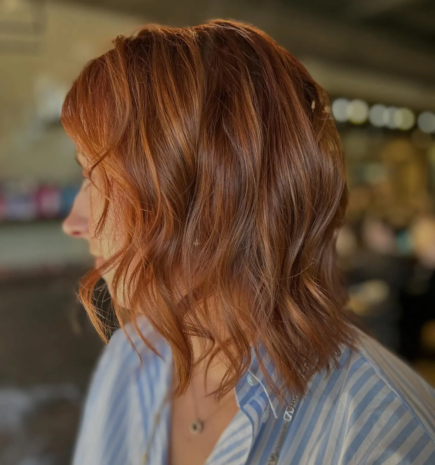 Warm copper wavy lob, client near-profile, warm venue bokeh